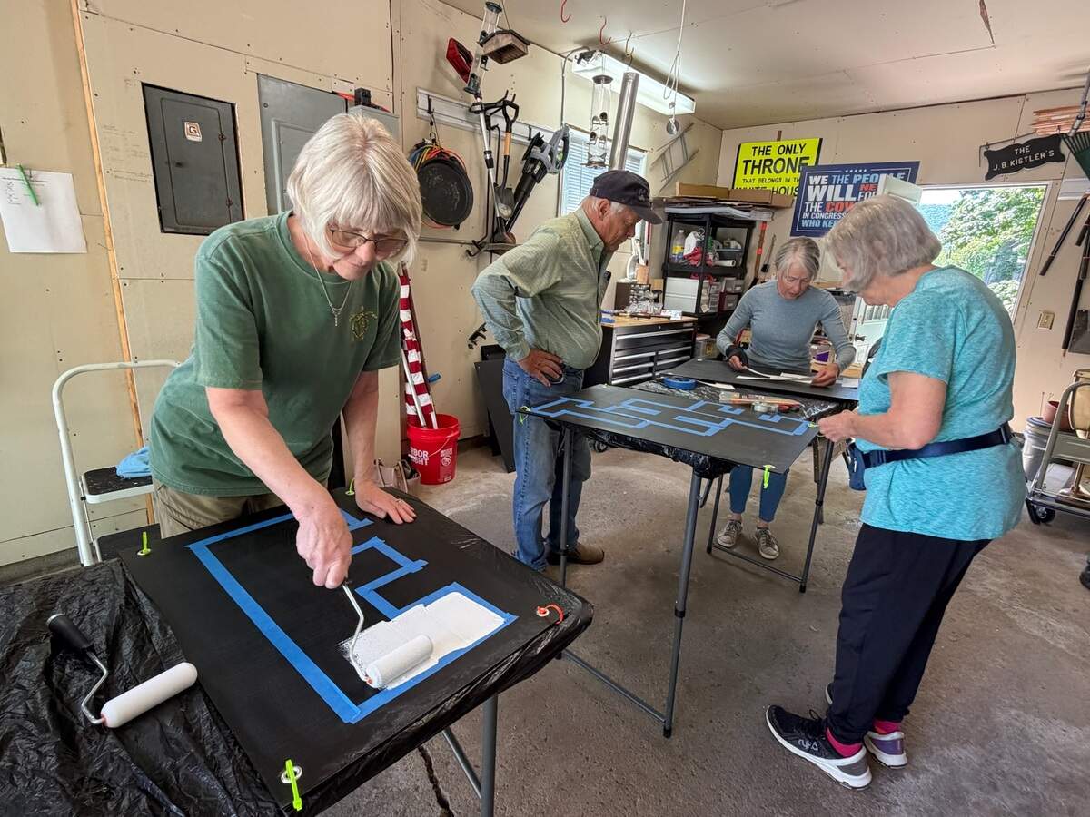 four volunteers gather in garage and paint, prepare black signs with white lettering and blue masking tape
