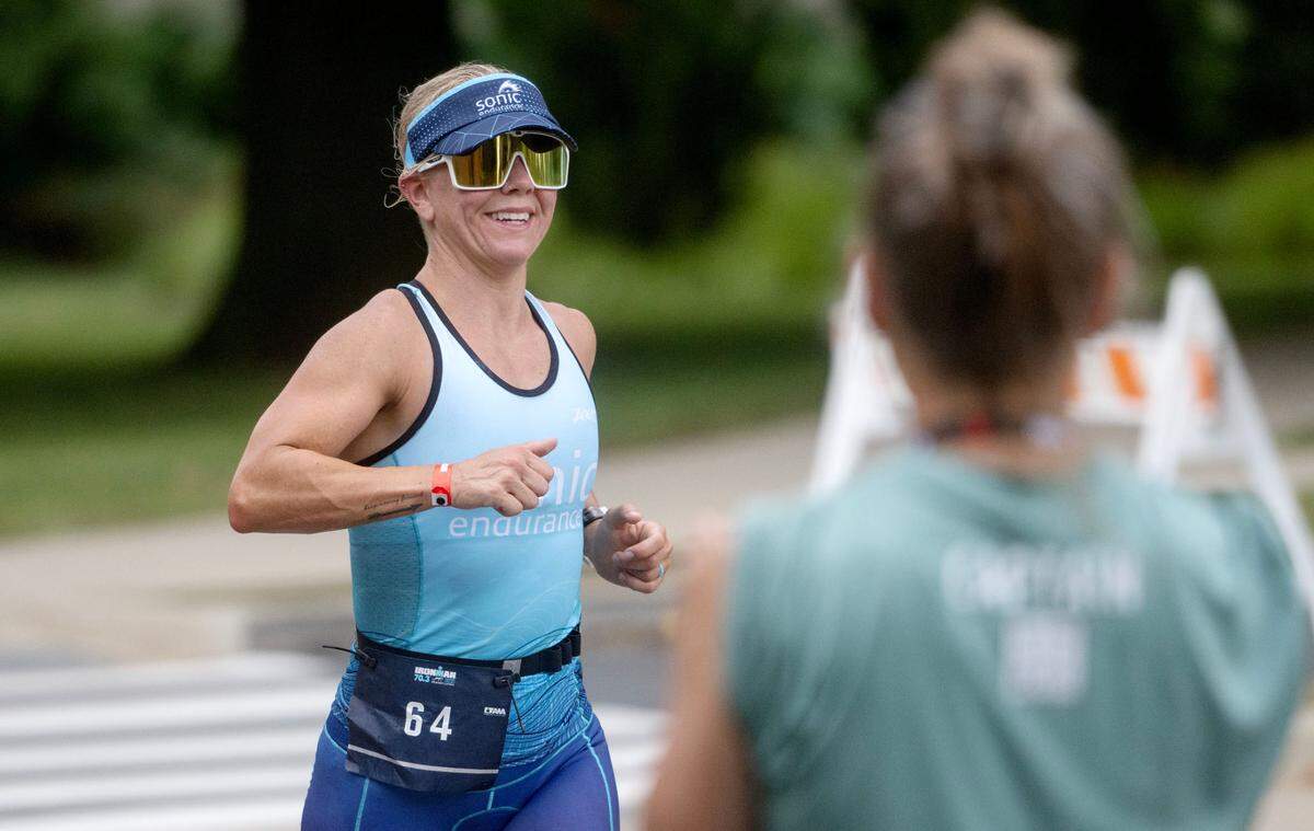 Athletes smile as they are cheered on by volunteers at water stations during the Ironman 70.3 Pennsylvania Happy Valley on Sunday, June 30, 2024.