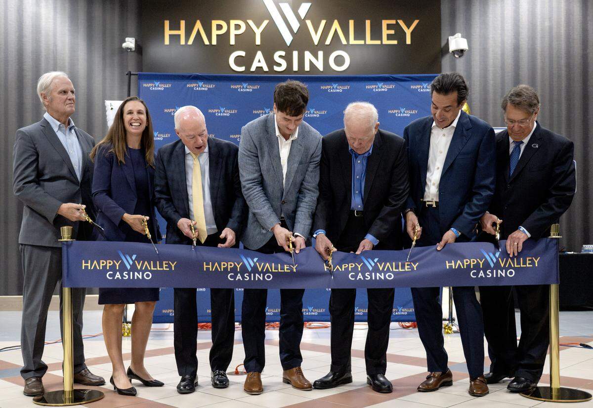 Sam Gerrity, CEO of Saratoga Casino Holdings, and Ira Lubert cut the ribbon for the Happy Valley Casino while surrounded by others involved in the casino. 
