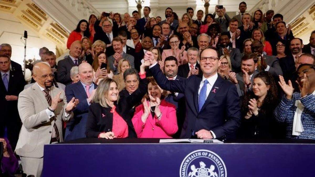Pa. Gov. Josh Shapiro holds up Senate President Pro Tempore Kim Ward’s hand as he signs the first bill of his tenure.