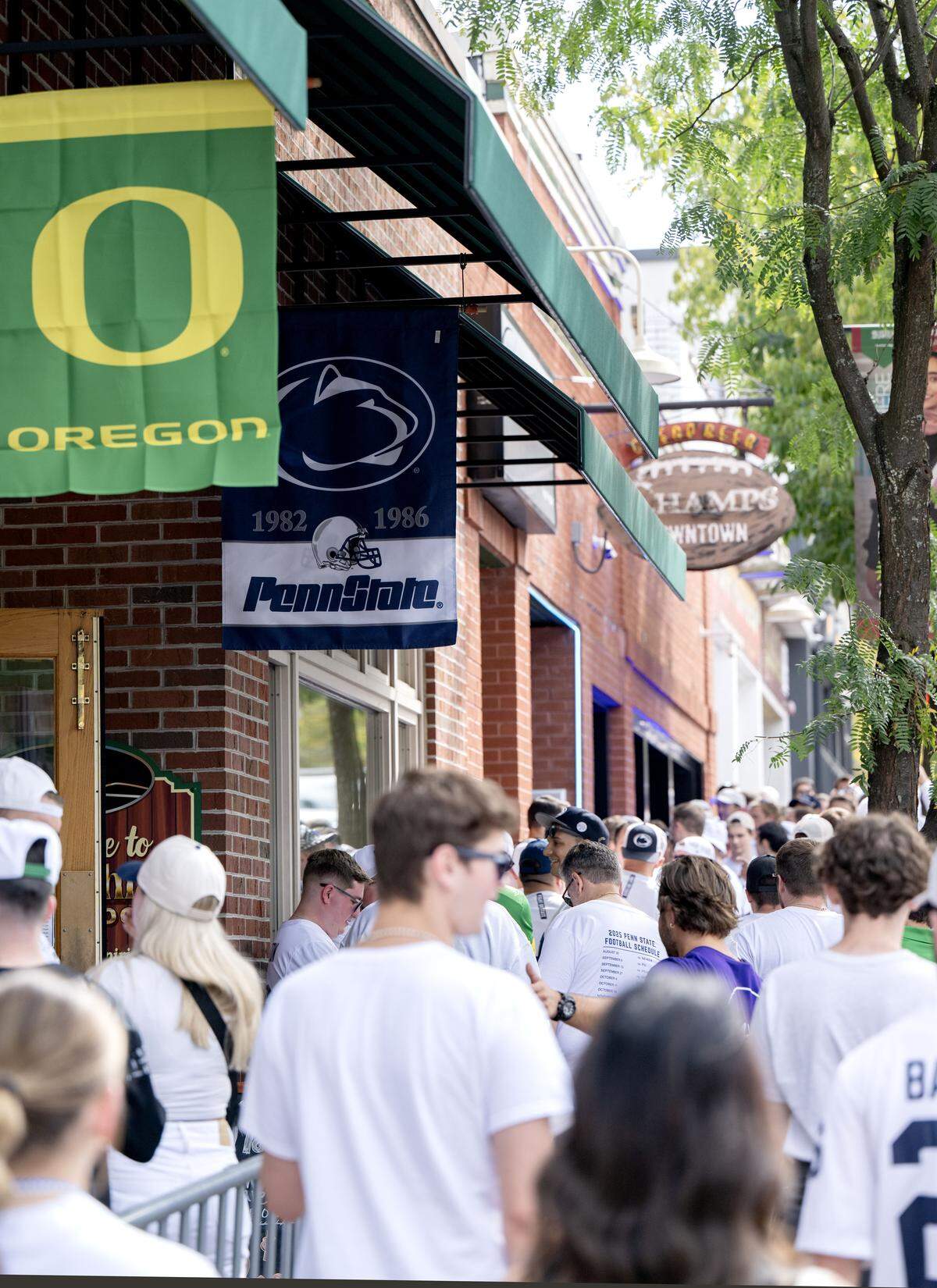 An Oregon flag and a Penn State flag hang outside of Appalachian Outdoors as fans fill the sidewalks along Allen Street before the game on Saturday, Sept. 27, 2025.  
