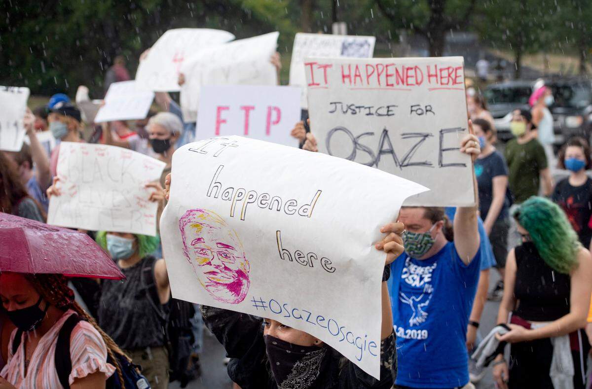 An advocate carries a poster that reads, it happened here with a sketch of Osaze Osagie as they stop traffic to walk down College Avenue in the rain on Saturday, Aug. 29, 2020. The 3/20 Coalition organizing the march and teach in.