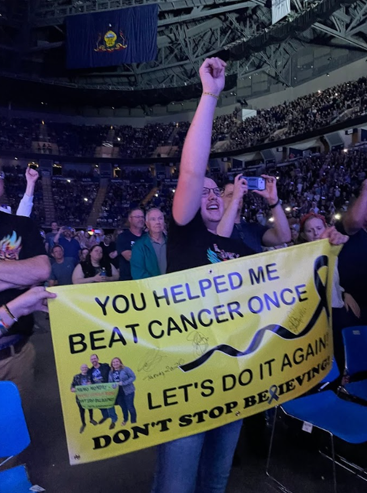 Cancer patient and nonprofit founder CJ Coudriet sings while holding up his banner at Wednesday’s Journey concert.