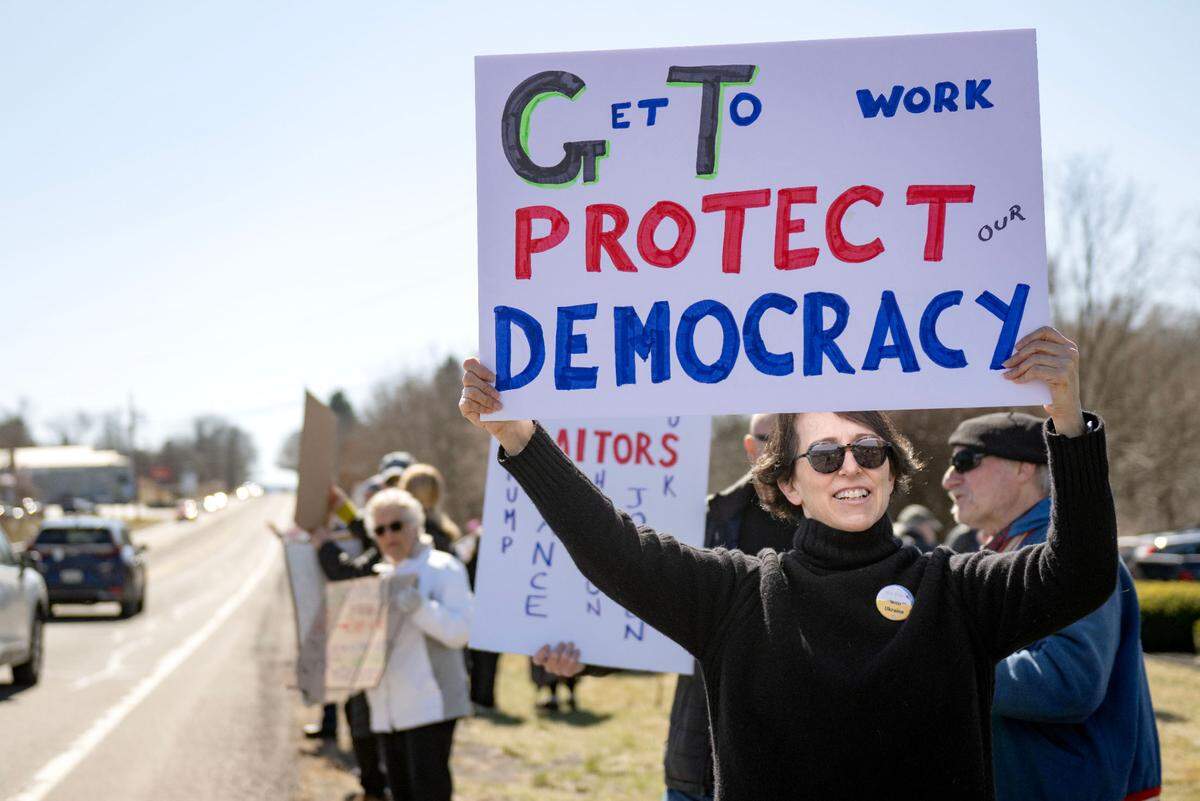 Joyce Furfaro holds a sign up as she stands with fellow protesters along Benner Pike outside of U.S. Rep Glenn “GT” Thompson’s office on Tuesday, March 18, 2025.