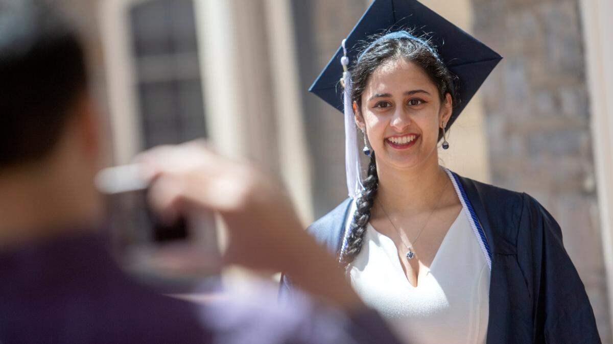 Nisha Moorthy smiles as her brother Neal takes graduation photos of her outside of Old Main on Friday. Moorthy and her family traveled to State College from Washington state to celebrate her 2020 graduation.