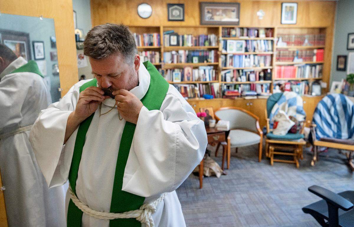 Senior Pastor Scott Schul kisses a cross medallion as he puts it on in his office at Grace Lutheran Church on Wednesday, Aug. 30, 2023.