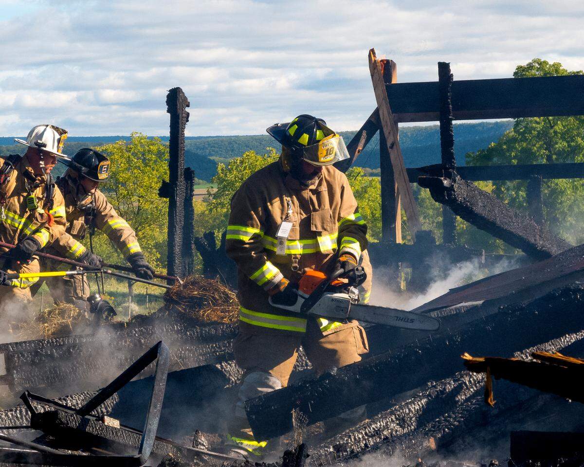 Matt Smith from Millheim cuts charred timbers with a chain saw after a barn fire a on Paso Lane in Penn Township. In the background are others going through straw looking for hot spots.