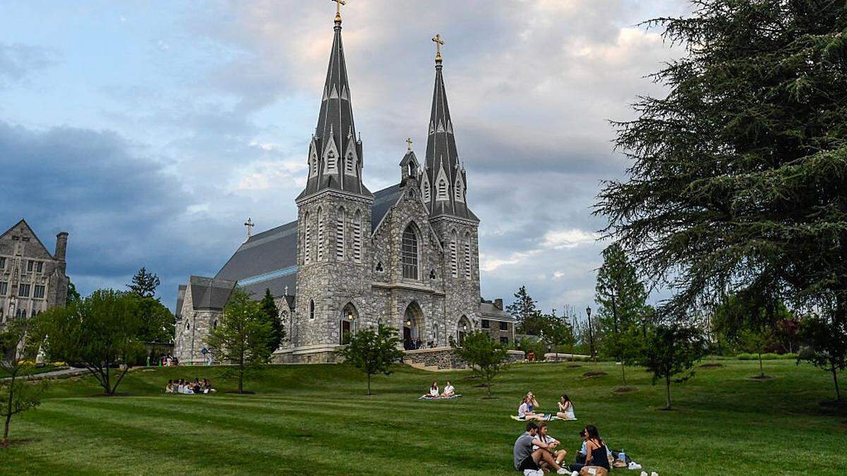 Students sit on the lawn outside of St. Thomas of Villanova Church at the campus of Villanova University in Villanova, Pennsylvania on May 8, 2025. Church bells rang as Robert Francis Prevost, a Villanova 1977 graduate, was elected the first pope from the United States on May 8, 2025, picking the papal name Leo XIV. (Photo by Matthew Hatcher / AFP) (Photo by MATTHEW HATCHER/AFP via Getty Images)          