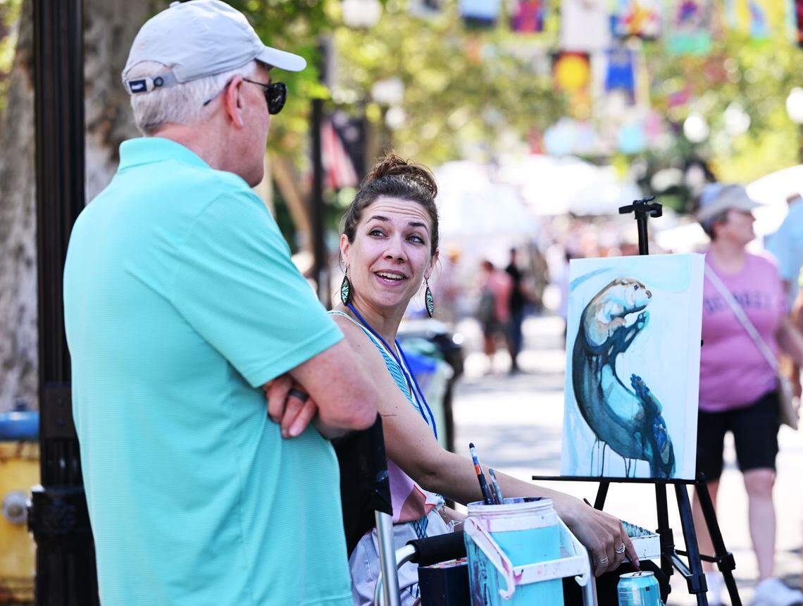 Kelsey Showalter (right) of Morgantown, Pa., discusses her artwork with Bill Hartman of Lancaster, Pa., at the 57th Central Pennsylvania Festival of the Arts, Friday, July 14, 2023. (For the CDT/Steve Manuel)