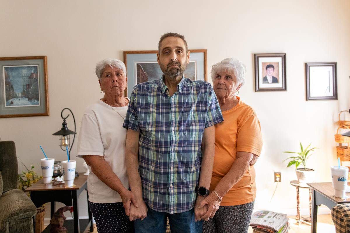 Conestoga Township, Pa: Troy Geiter stands in the living room with his mother, Dorothy Long, left, and his aunt, Carol Waltman, right. in Conestoga Township on Monday, September 9, 2024. Troy needs a second liver transplant and is one of many patients that were part of the suddenly shuttered Penn State Health transplant program. Troy said his mom and aunt have been with him through this since day one.