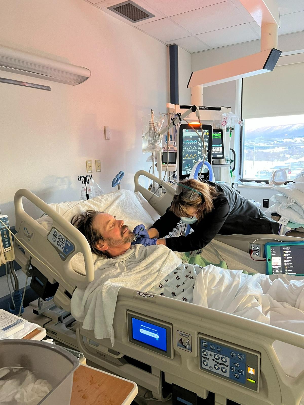 A nurse shaves Ted Edwards as he lies in a hospital bed in the COVID unit at Mount Nittany Medical Center in January of 2021.