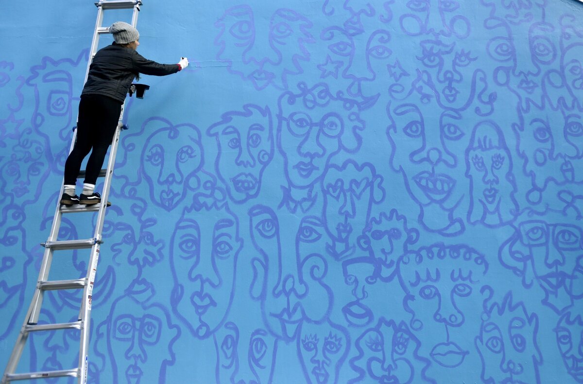 Penn State freshman Lucy Udell paints her contour portraits on the side of the State Theatre on Tuesday, Oct. 30, 2018. William Snyder III helped to paint the portraits, and will do more work on the mural.