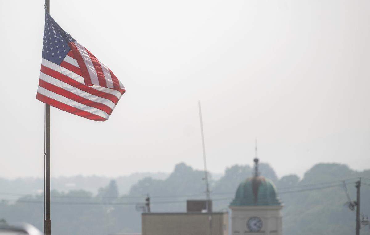 A flag waves outside of the sheriff’s office but smoke and haze distorts the view of the courthouse clock tower and beyond on Thursday, June 29, 2023.