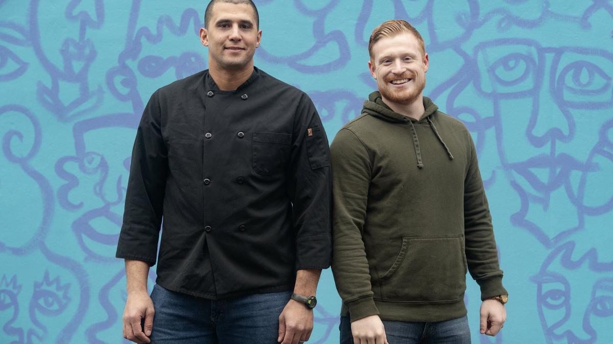 Open Seat founders Thomas Novosel Jr. and Tim Parker pose Wednesday in front of a mural by William Snyder III on Calder Alley in downtown State College.