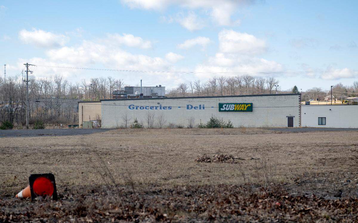 A road cone lays in the field Thursday, Feb. 23, 2023, next to the empty building that formerly housed Hall’s Market, True Value, Subway and Jersey Shore State Bank.