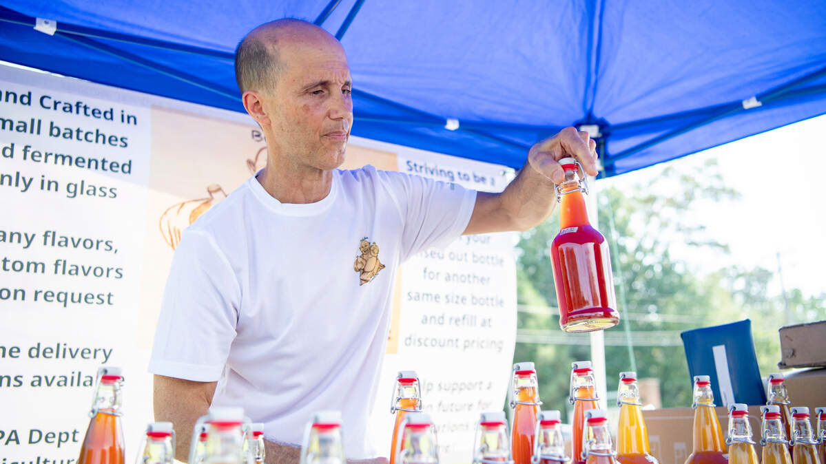 Chris Kepler of Buddha Kombucha gets a bottle for a customer at the Pine Grove Mills farmers market on Thursday, Aug. 12, 2021.  
