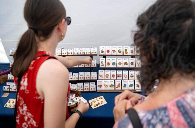 Guests browse the wooden earrings and pins hand painted by Amanda Jones in her Teaberry Design Co. booth at the People’s Choice Festival on Friday, July 14, 2023.