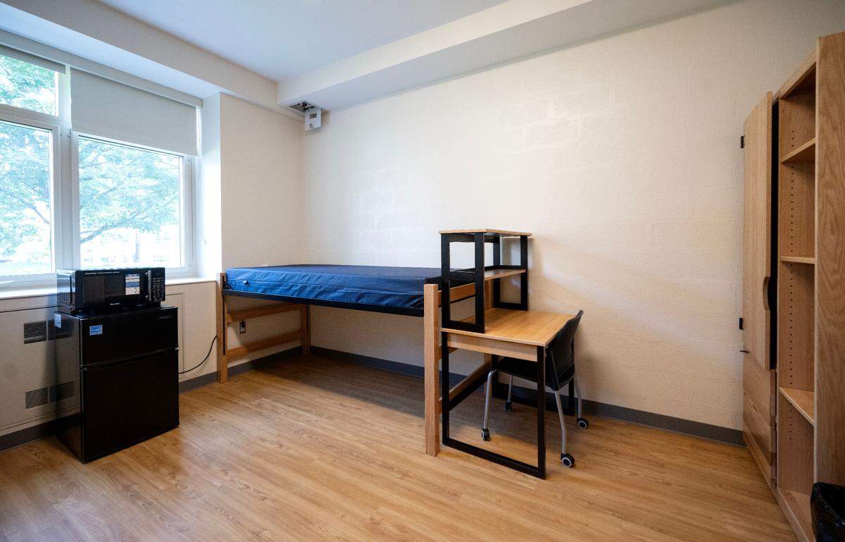 One side of a double occupancy dorm room in Hastings Hall with an adjustable height bed, desk, closet, mini fridge and microwave.