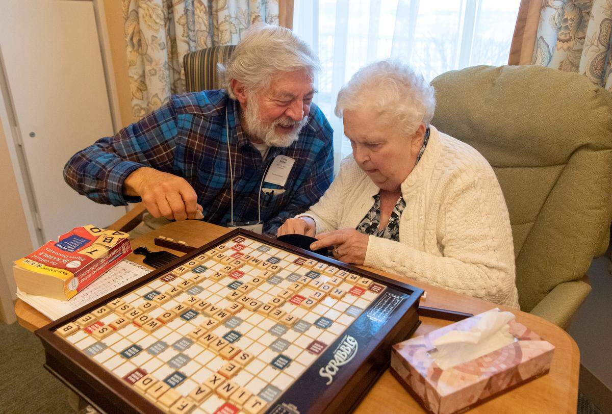 Doug Miller laughs with his wife, Grace, as she finds the letter she needs for the next word in a game of Scrabble in her room at Foxdale Village on Thursday, Dec. 16, 2021.