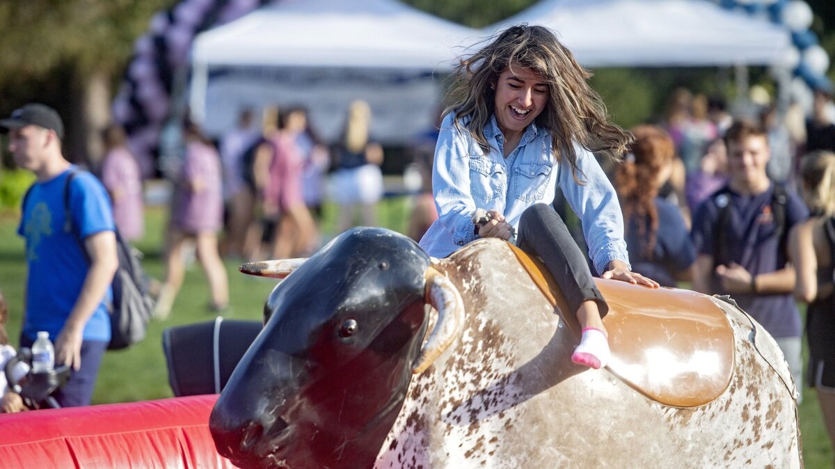 Penn State student Marielena Rodriguez laughs as she tries to hold on to the mechanical bull in October 2018 during the Penn State Homecoming Carnival on the HUB Lawn.
