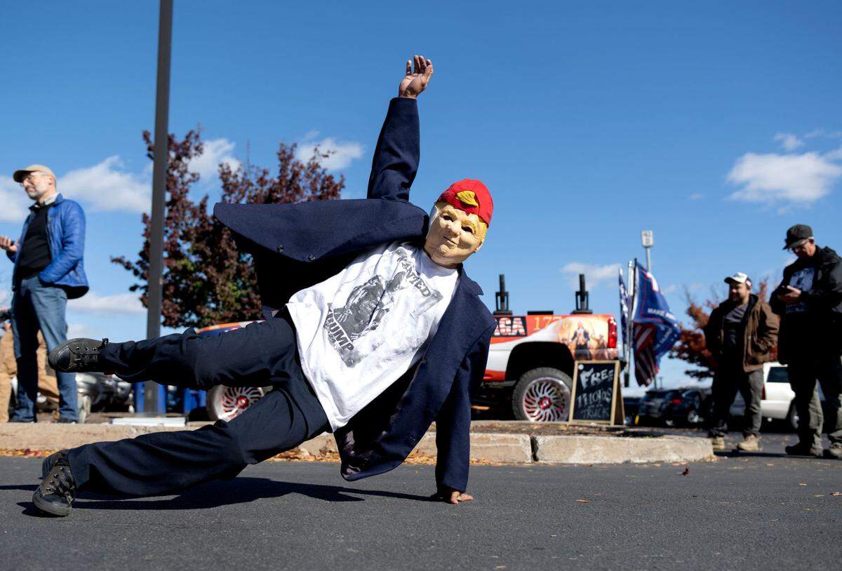 A breakdancer wears a Trump mask as he performs for outside of the Bryce Jordan Center before the rally on Saturday, Oct. 26, 2024.