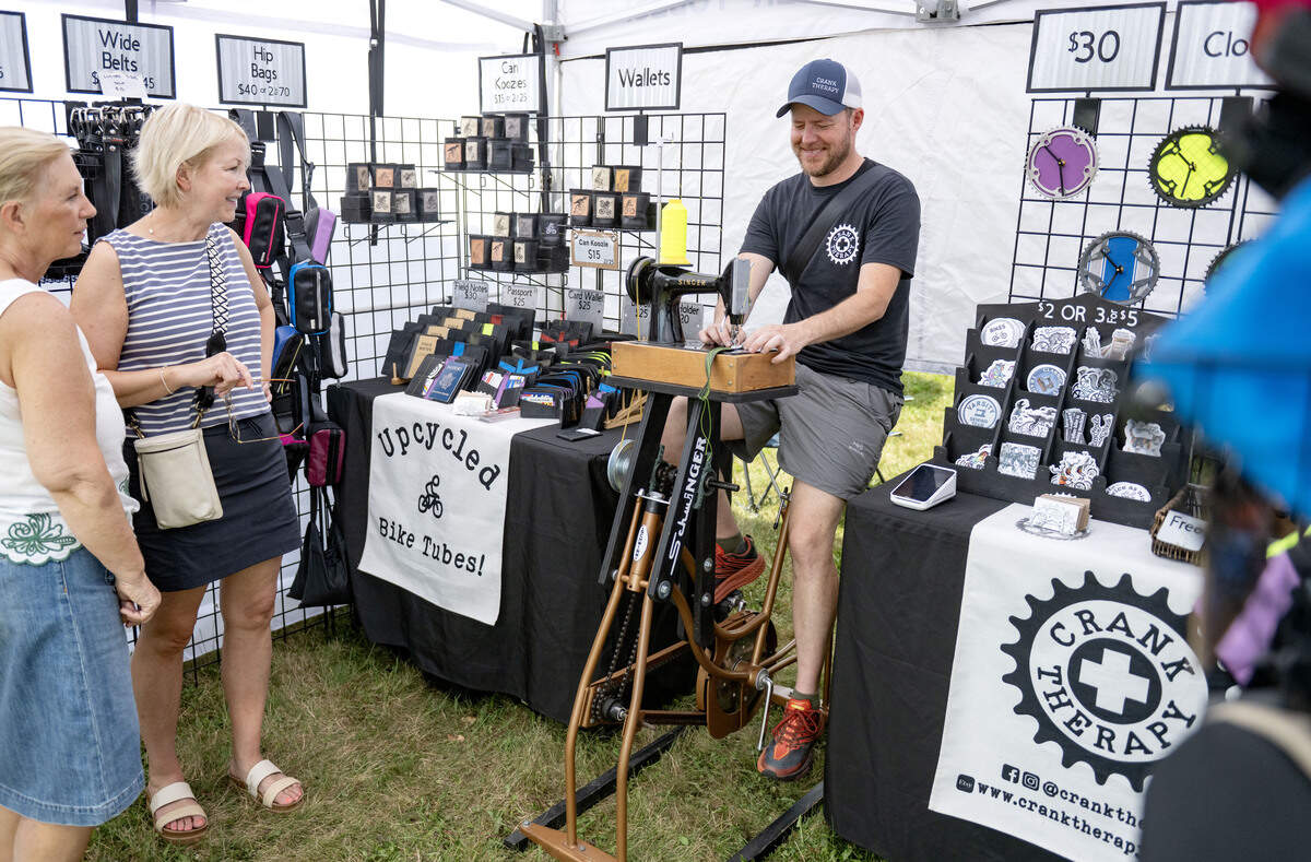 Ben Masters chats with customers as he rides his ”Schwinger,” a Schwin bike that powers a Singer sewing machine when pedaling, at the People’s Choice Festival on Thursday, July 9, 2026. Masters’ booth Crank Therapy sells items sewn for recycled bicycle inner tubes.