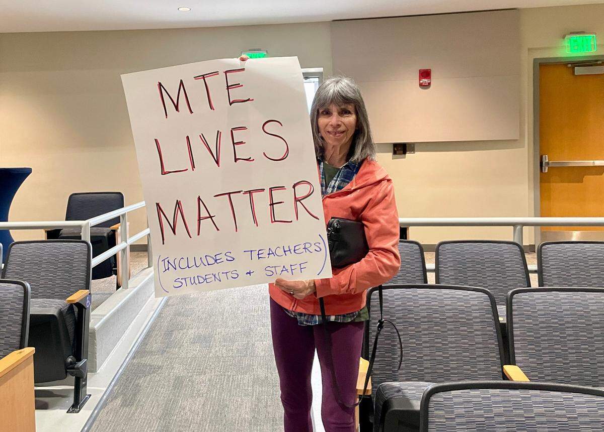 Sarah Berndt poses with a handmade sign at a public hearing for the potential closure of Miles Township Elementary. She said she received the sign from another guest in attendance but supports its message.