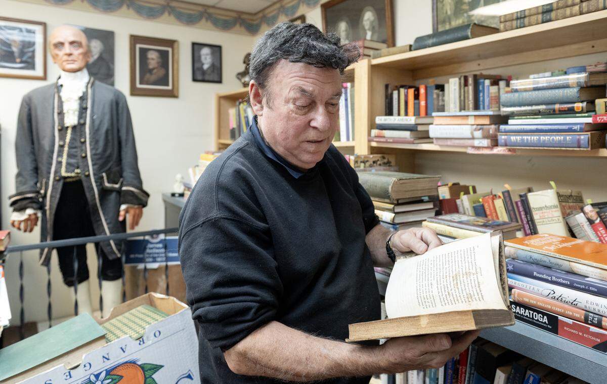 Keith Bierly of Forefathers Book Shop flips through a book that is part of a collection about the signers of the Declaration of Independence on Thursday Sept. 4, 2025. Behind him stands a statue of James Madison.  