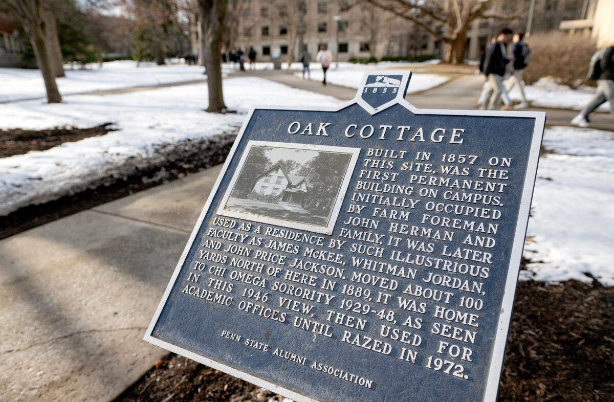Students pass by the Penn State Alumni Association historical marker for Oak Cottage.