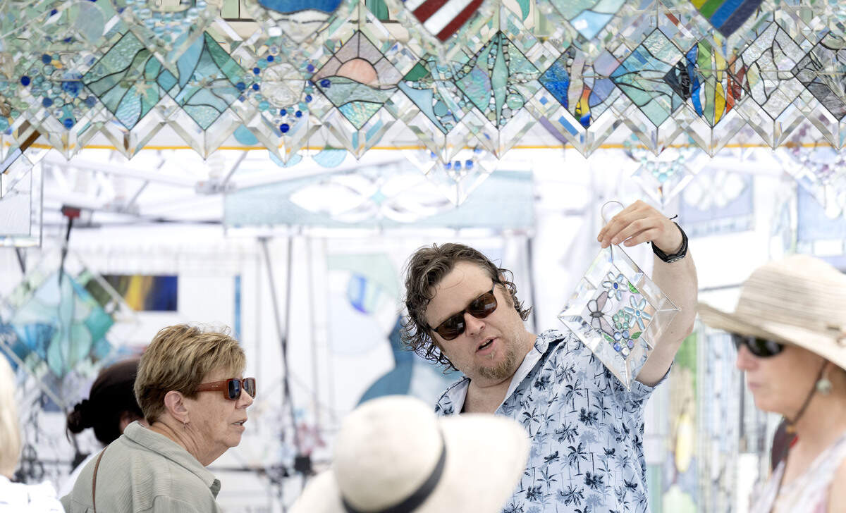 Kyle Hamm shows a customer a stained glass piece in he and Tiny Feldi’s booth Progressive Expressions at the People’s Choice Festival on Thursday, July 9, 2026.