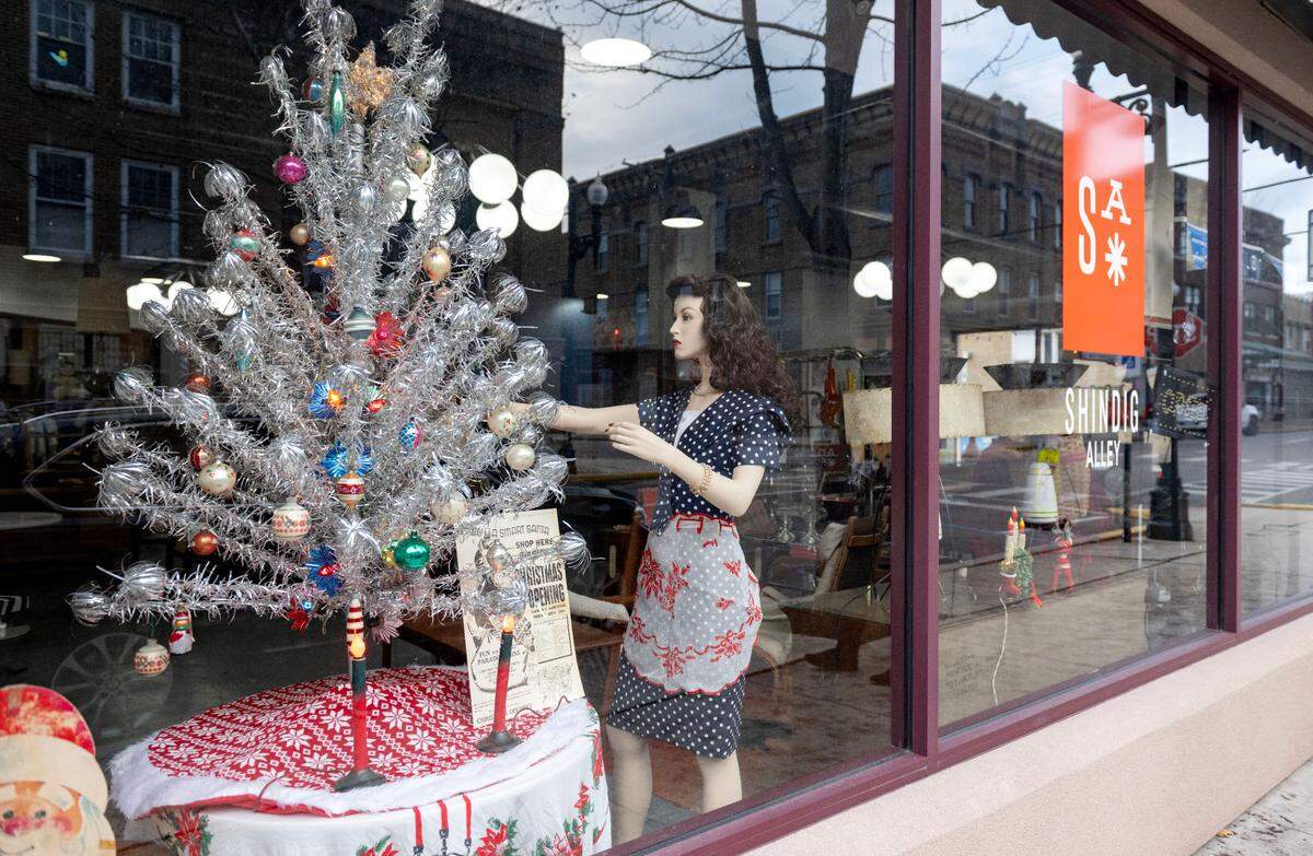 A window display at Shindig Alley features a mannequin decorating a trumpet tinsel tree. Storefronts along North Front Street are decorated for Philipsburg’s Mid-Century Christmas.