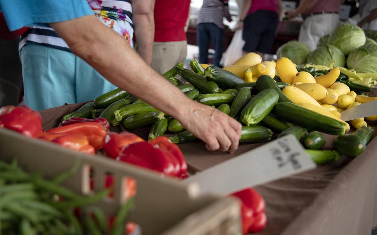 A man picks a zucchini at the Hills Plaza farmers market on Tuesday, July 16, 2019.
