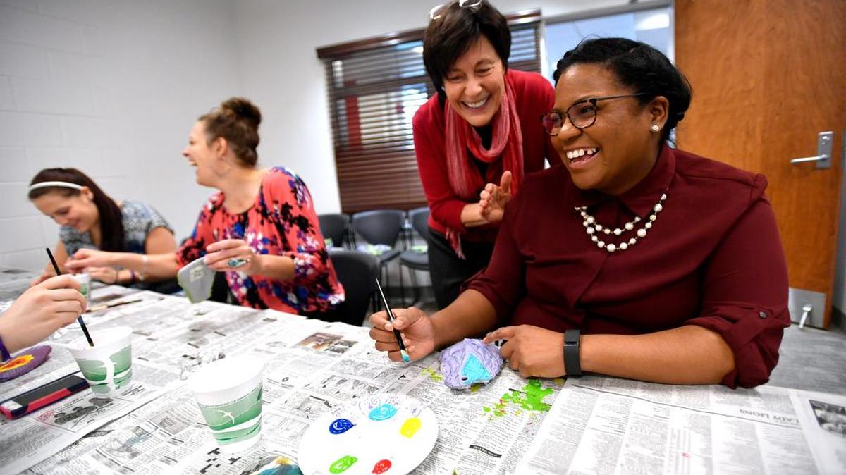 Jo Lynn Carney, middle, and Jessica Henry, right, laugh while painting pieces of shoes for the Stompers Project on April 12. The Cedar Clinic teamed up with the Jana Marie Foundation to make a “stomper” to promote suicide awareness and prevention.