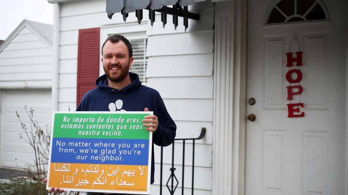 Penn State campus pastor of 3rd Way Collective Ben Wideman holds up one of the signs he brought to the area. In three languages, the sign says, “No matter where you are from, we’re glad you’re our neighbor.”
