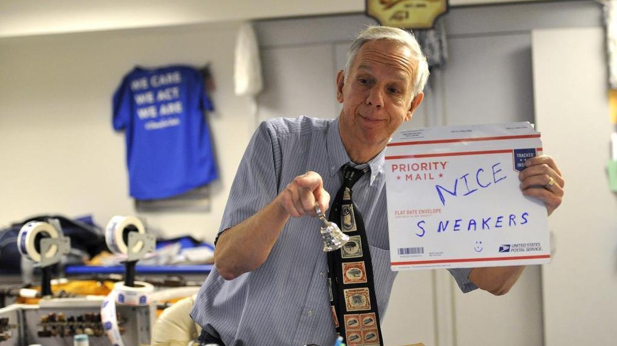 Mike Herr holds up a sign and rings a bell as a girl with colorful shoes walks into the post office. Mike Herr, otherwise know as “Mike the Mailman,” serves customers in the post office located on the Penn State University campus February 4, 2016. Herr has been working for the United States Postal Service for the last 47 years.
