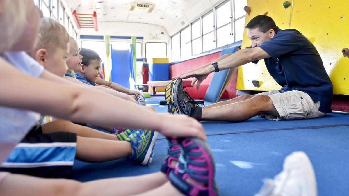 Chris Deyo leads a group to stretch as they play in Tumblebus during its stop at the Abba House on Tuesday. A rock wall, slide, zip line, balance beam and more fill the padded bus.