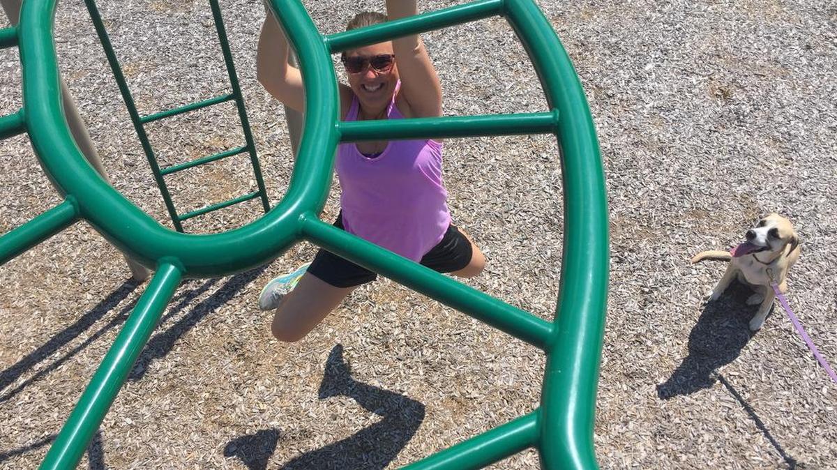 Abby Drey, with dog Stella in the background, climbs the monkey bars at Cecil Irvin Park in Ferguson Township to fulfill one of the requirements of the Centre Region Parks and Rec’s Park Picture Pursuit Photo Scavenger Hunt.