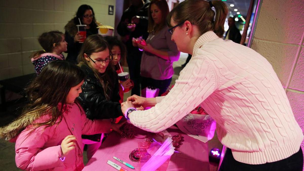 Tracy Carey gives GIrls Scouts Madison Judy, 7, left, and London Judy, 10, glow-in-the-dark bracelets on Sunday before a special showing of the movie “Hidden Figures” at College 9 State College.