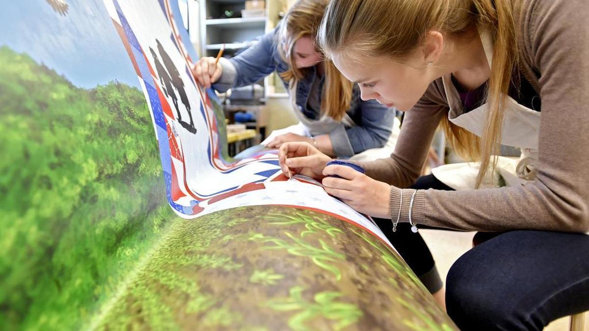Bald Eagle Area students Lexi Turner and Sara Snyder paint a section of the book bench on Thursday. More than 100 students helped to paint the bench with farm scenes, an eagle and a detailed quilt.
