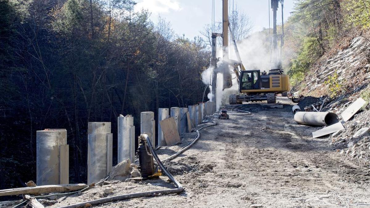 Dust and water vapor fill the air where workers drill to set a steel piling as work continues on Purdue Mountain Road in Benner Township on Thursday. Parts of the road were washed out from flooding last October.