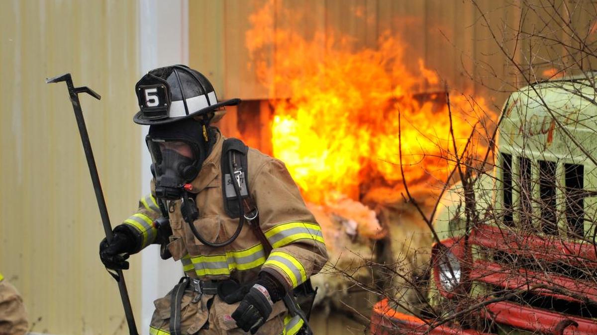 A firefighter moves out of the way as flames burn behind. Firefighters battle a structure fire at Gray’s Vehicle Clinic in Axemann Feb. 25, 2016.