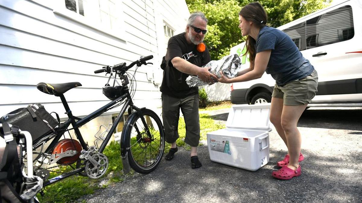 Melanie Rosenberger hands Chip Mefford a bag of food to be delivered by bicycle during the Friends and Farmers Cooperative Online Market’s Bike Delivery Day in May. The co-op is looking to establish a brick-and-mortar store.