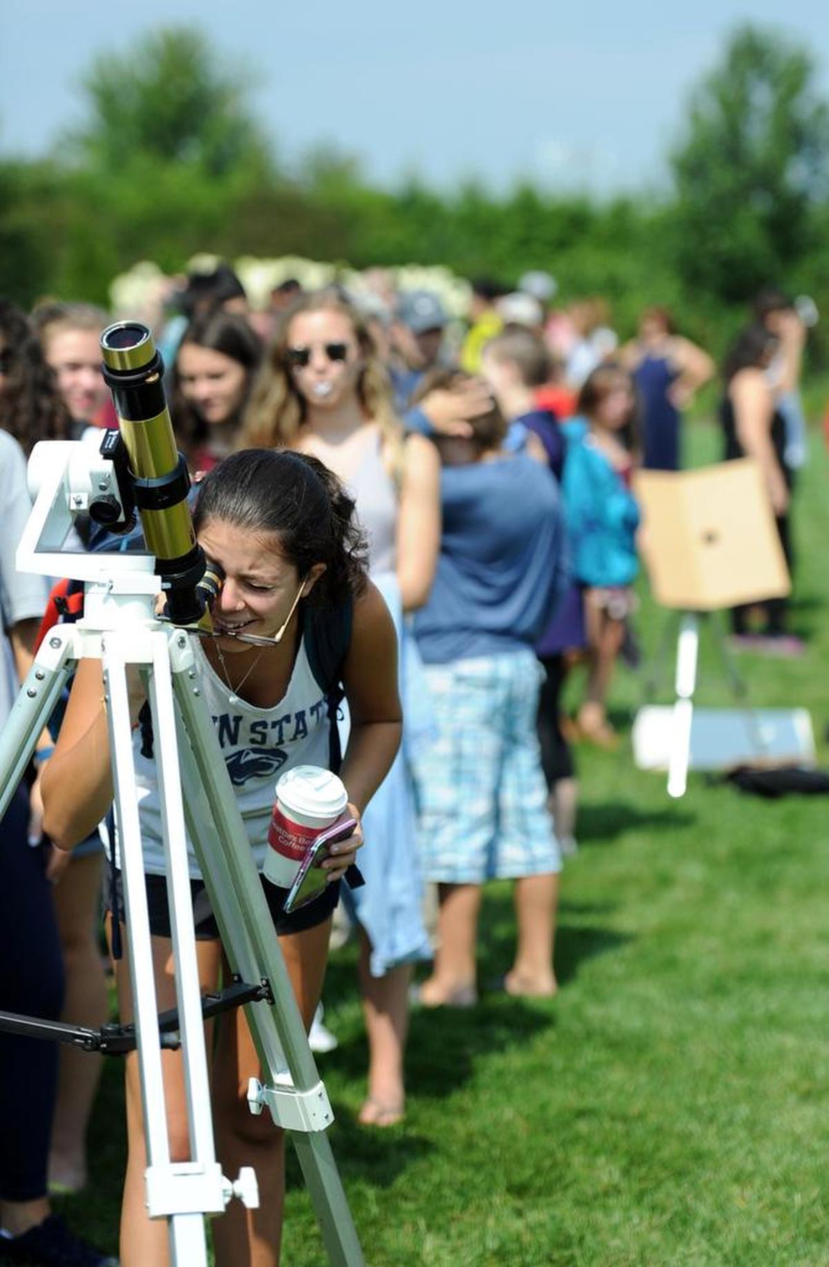 A line of people await to view the eclipse through a telescope as Amber Wingate takes her turn Monday, Aug. 21, 2017 at The Arboretum at Penn State.