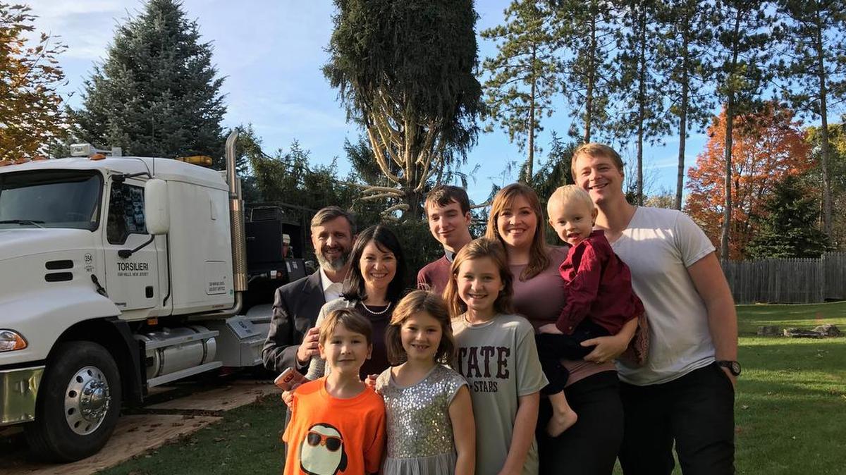 Kristina Whitaker and Lisa Strickland pose with their families in front of the 75-foot-tall Norway spruce that would soon become the Rockefeller Center Christmas tree. Their father, Hal, who had just died a few days prior, grew up in a home near the tree.