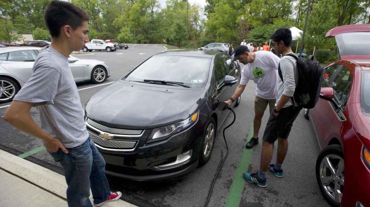 Darren Schilberg demonstrates how to use the charging station to Penn State students Aaron Herschlaz, left, and Nikhil Bharadwaj during the National Drive Electric Week event on Sunday at the Country Inn and Suites in State College.