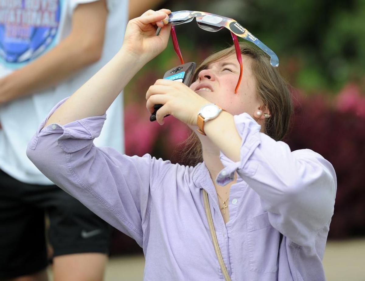 Jessica Brunbaugh takes a picture of the eclipse with her phone through her glasses Monday, Aug. 21, 2017 at The Arboretum at Penn State.