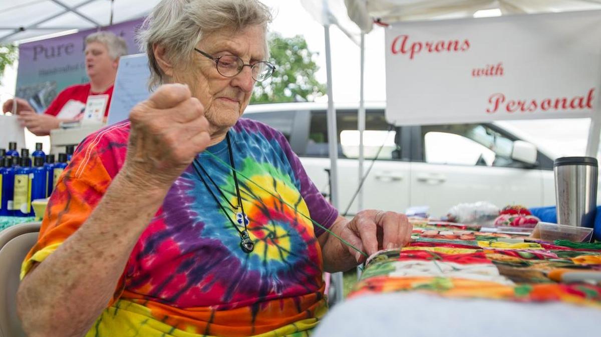Edna Kotrola sews a backing for her “Aprons with Personality” tent during FarmFest at the Grange fairgrounds on Friday.