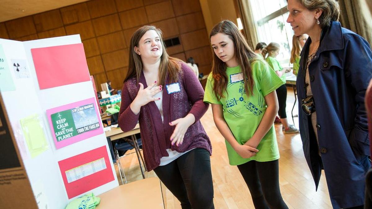 Cassie Fults, left, and Jillian Packer, center, of the Bald Eagle Area School GAMES Club, introduce their wind turbine project to Kristine Dreyer, from AAUW State College, on Wednesday during the KidWind Challenge event on Penn State’s campus.