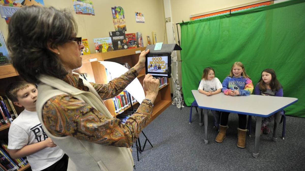 Reading specialist Mary Conner-Righter films students on Monday for a mock television broadcast based on a book the students have read. The Miles Township Elementary School library had a flood last year causing major damage. The library has since been renovated, and the students are using it again.