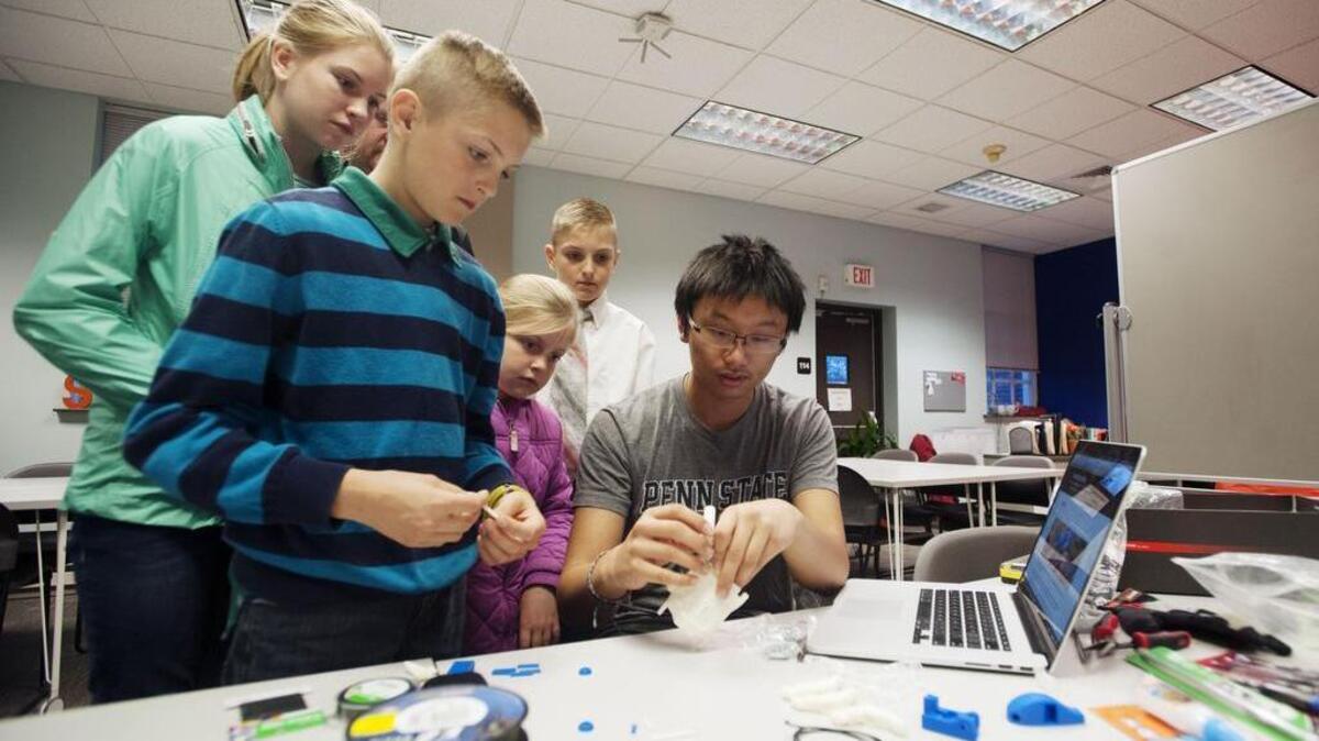 Penn State junior Ryan Lo, far right, shows Isaac Rose, 11, Annabelle Rose, 12, Liliana Rose, 7, and Alexander Rose, 11, a 3-D printed prototype hand during a Digi Digits workshop Monday at Happy Valley Launch Box in State College.